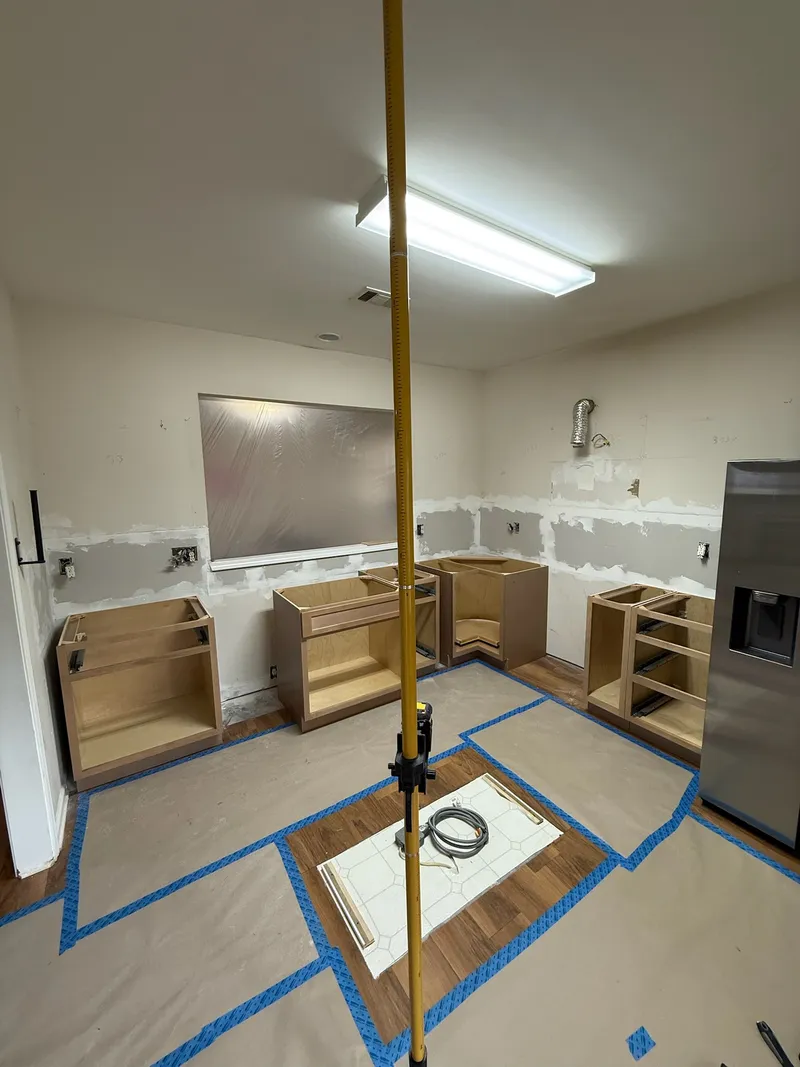 Anchor & Grain kitchen installation in progress — cabinets being set with floor protection and laser-level layout.