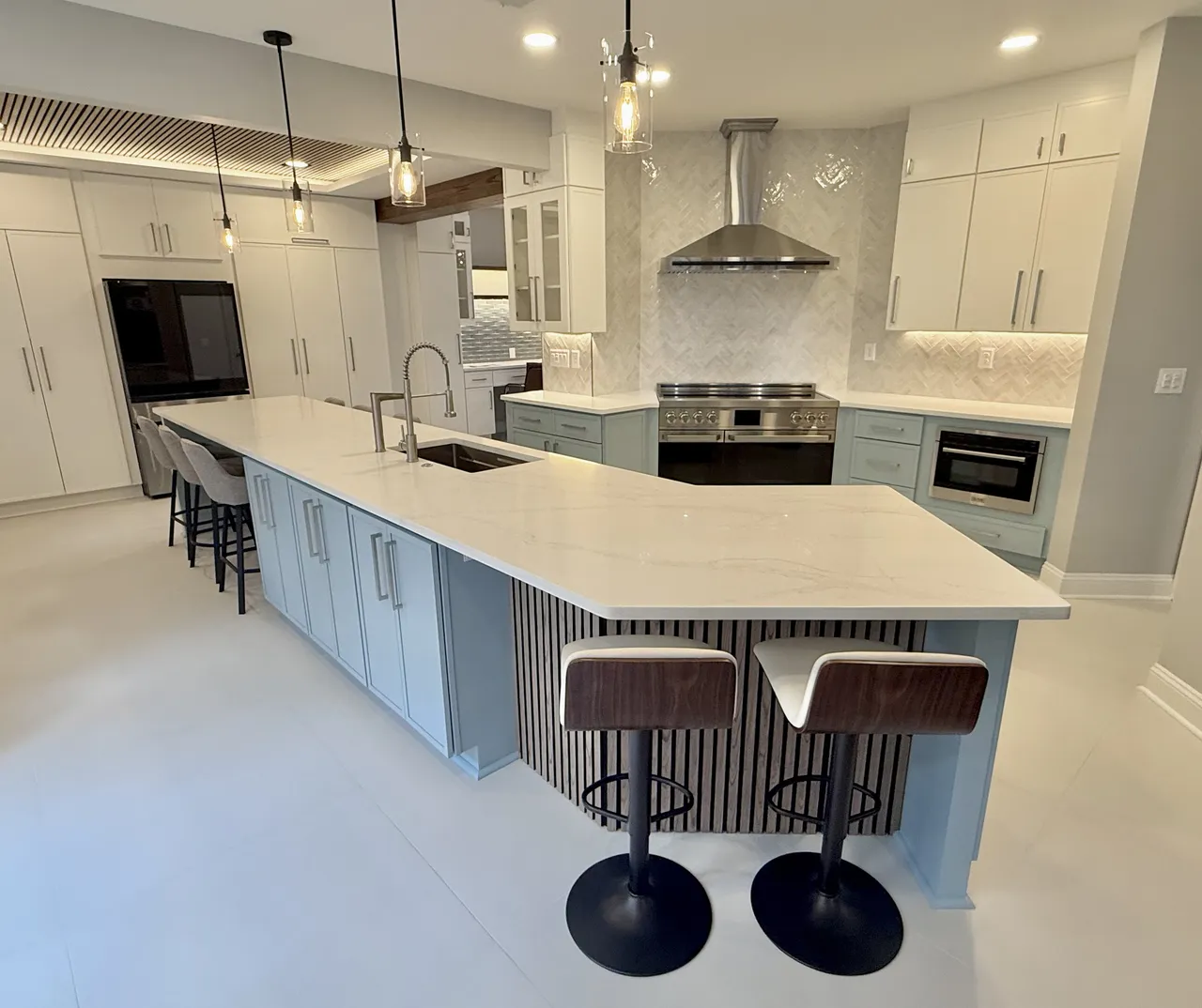 Custom kitchen remodeled by Anchor & Grain in North Atlanta — light blue island, quartz counters, herringbone backsplash, and a stainless range.