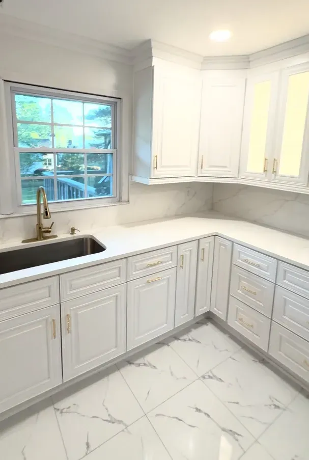Renovated kitchen with classic white raised-panel cabinets, calacatta-look quartz countertops, brushed brass faucet, and marble-pattern tile flooring.
