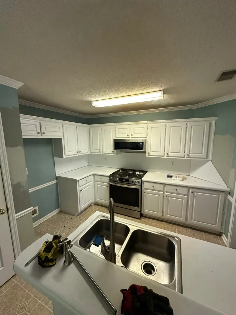 Kitchen during construction, walls stripped to drywall and floor stripped to subfloor, with utilities exposed.