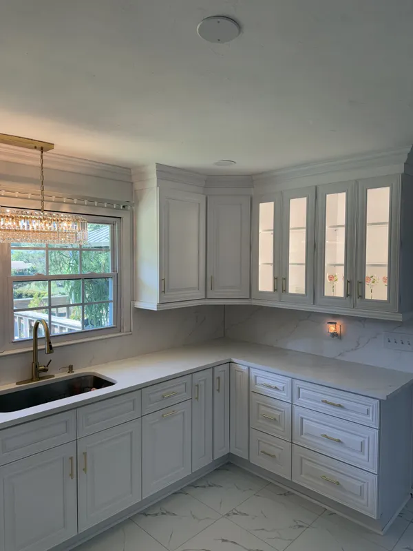 Finished kitchen with classic white raised-panel cabinets, calacatta-look quartz countertops, brushed brass fixtures, and marble-pattern tile flooring.